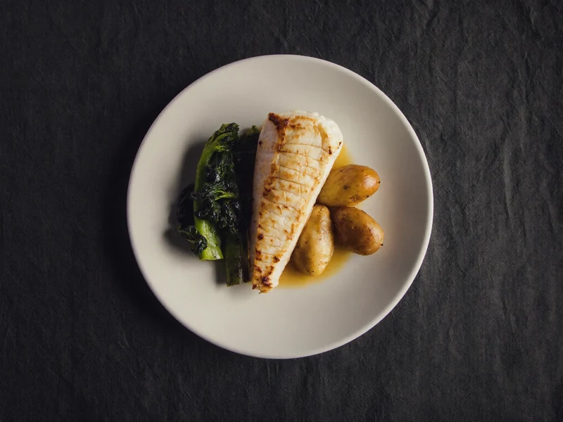Pesce bianco al forno con verdure al vapore e patate lesse su piatto semplice